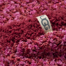 Close-up of a chunky, textured knit beanie in a variegated pattern of deep red, burgundy, and magenta pink, featuring a beige fabric UGG logo tag.