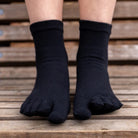 Black ribbed toe socks worn on a person's feet, shown from the toes up against a blurred wooden slatted background.