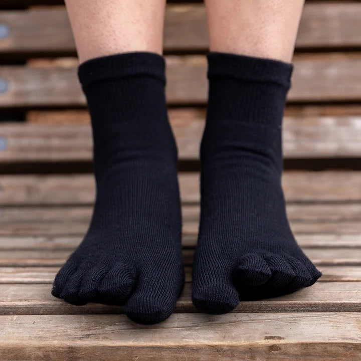 Black ribbed toe socks worn on a person's feet, shown from the toes up against a blurred wooden slatted background.