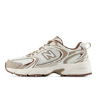 A New Balance 530 sneaker in a cream, beige, and brown colorway, shown from a side profile view against a plain white background.