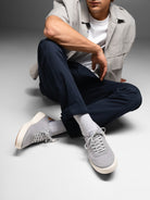 Person wearing gray sneakers, navy pants, and a light gray jacket sitting on a white surface.