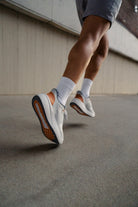 Person wearing white sneakers and gray shorts on a concrete surface.