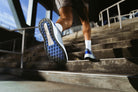 Person climbing stairs wearing blue running shoes with white soles.