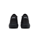 A pair of black low-top sneakers shown from the back, featuring a matte black upper and thick black sole with a small gray reflective accent on the heel.