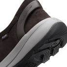 Close-up of a Kizik slip-on shoe showing the dark brown suede upper, a gray midsole, and a black textured outsole with Kizik branding.