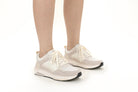 A pair of low-top athletic sneakers in off-white, beige, and light gray, shown on a model's feet against a clean white background.