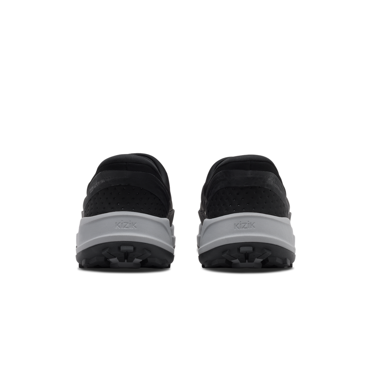 A pair of black slip-on shoes shown from the back, featuring a textured black upper and a thick light gray midsole with the brand name 'KZIK' embossed on it, set against a plain white background.